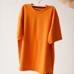 Bright orange t-shirt on a hanger against a plain background, perfect for fashion themes.