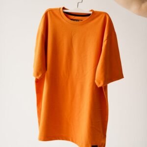 Bright orange t-shirt on a hanger against a plain background, perfect for fashion themes.