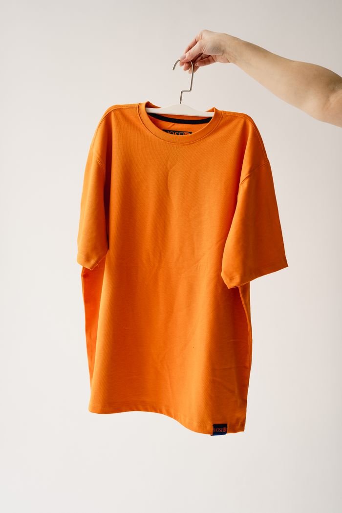 Bright orange t-shirt on a hanger against a plain background, perfect for fashion themes.