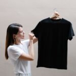 Side view of positive female wearing casual outfit standing with black shirt against gray background