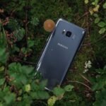 Close-up of a Samsung smartphone nestled in vibrant green leaves and moss.